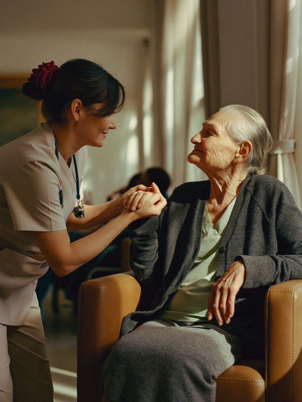 Caregiver holding hands with an elderly woman in a sunlit assisted living common room